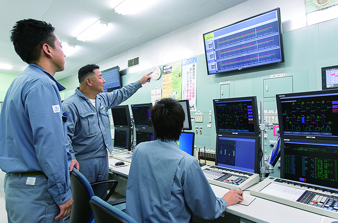 Instrument panel room for monitoring the entire operation of the anone manufacturing plant. The large 65-inch monitor is installed above the APS5000 monitoring/control panel. The monitor displays the APS5000's monitoring screen during normal operation. When an alarm is generated, the display automatically changes to the ACTMoS's monitoring screen. All members present in the room can grasp the condition of the generated abnormality so that they can conduct response activities in cooperation.