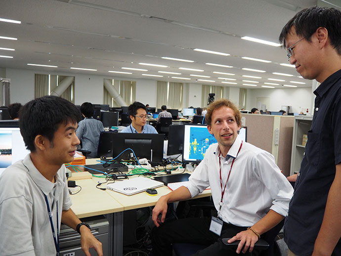 Alexander Payovich from Serbia (seated) is currently active in an R&D department as an intern. Interns discuss the details of their work with Azbil employees, who provide guidance.