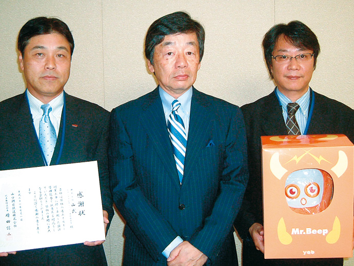 口朝日放送では、一連の環境問題への取組みが、自社の社会的な企業イメージの向上につながったことを高く評価。今回の省エネ施策、補助事業の申請を支援した山武に対して感謝状を贈った。山口朝日放送の増田信二社長(中央)と山武のスタッフ。